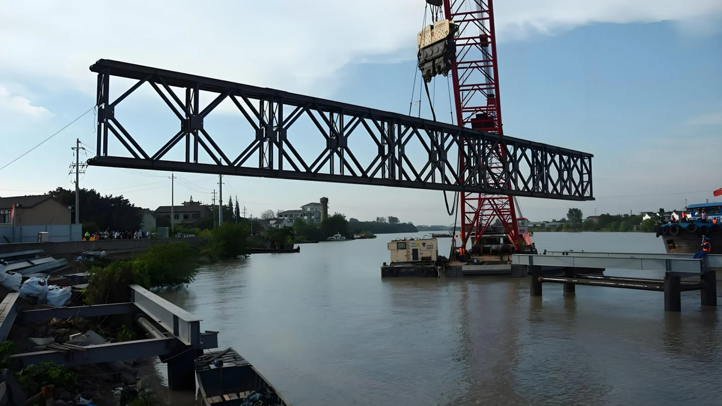Crane lifting a Bailey bridge truss section at a water crossing