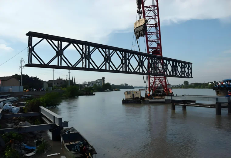 Crane lifting a Bailey bridge truss section at a water crossing